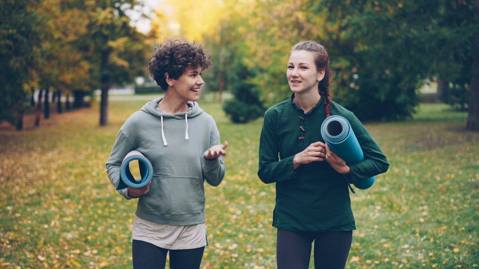 Twee vrouwen lopen met hun matje door een herfstpark en praten
